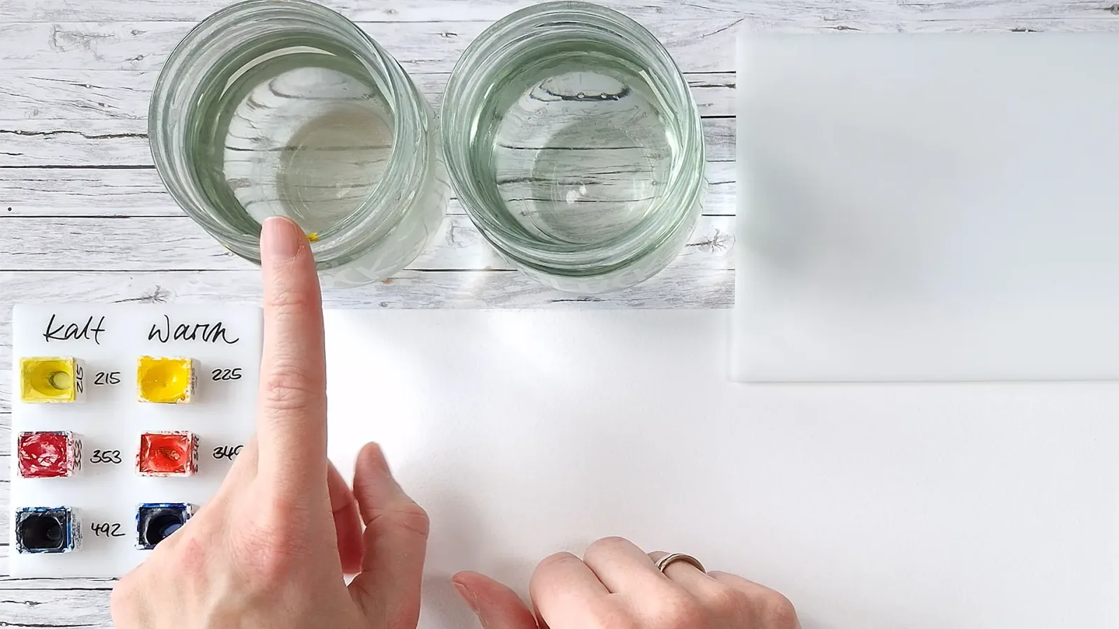 Zwei Gläser mit Wasser und Farbmuster-Proben zur Aquarellmischung auf Holzuntergrund
