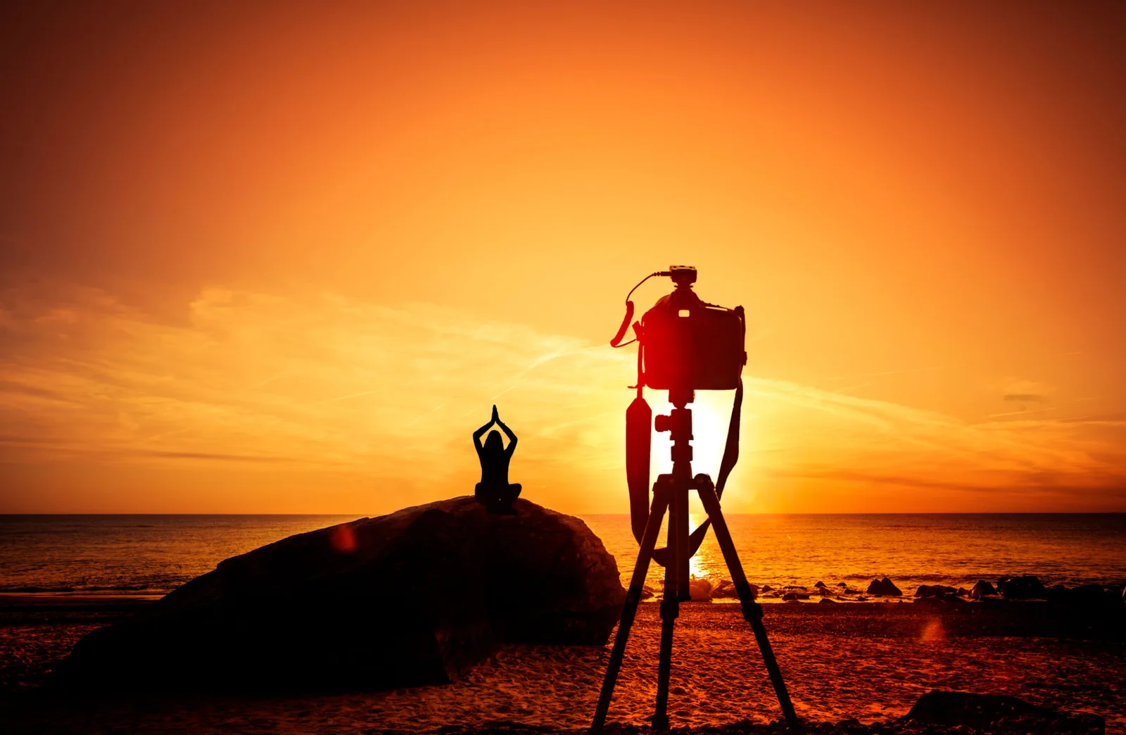 Silhouette: Fotografin mit großformatiger Kamera auf Stativ bei Sonnenuntergang am Strand