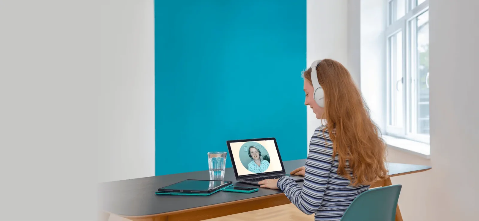 Frau mit Kopfhörern beim Online-Kurs-Studium am Laptop, modernes Büro mit türkiser Wand