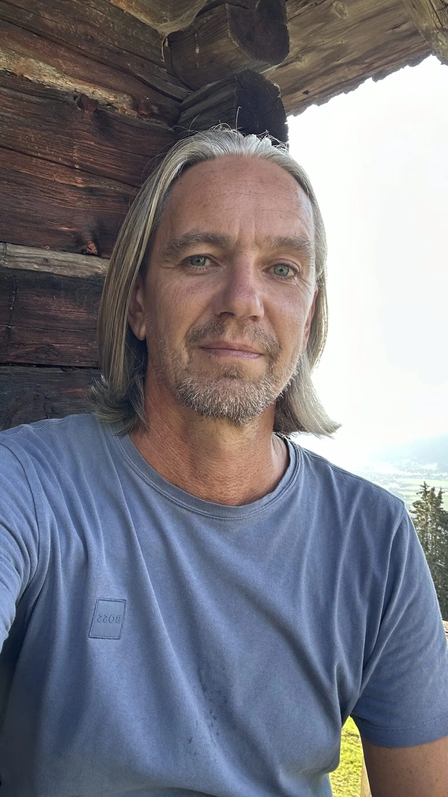 Mann mit langen grauen Haaren vor Holzhütte, Porträt