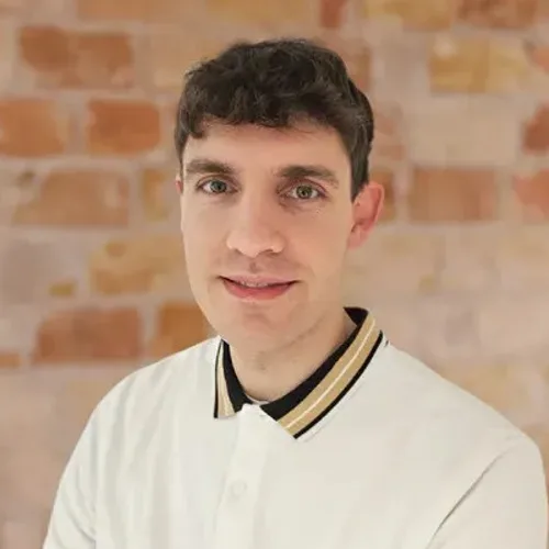 Tom, junger Mann mit dunklem Haar in weißem Hemd vor Backstein-Hintergrund