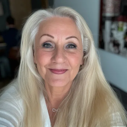Porträt Frau mit langen grauweißen Haaren, Make-up, weißes Oberteil, freundliches Lächeln