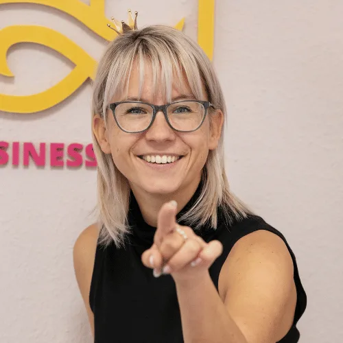 Porträt Julia Bock, lächelnde Frau mit Brille und rötlichem Haar, zeigt auf Kamera