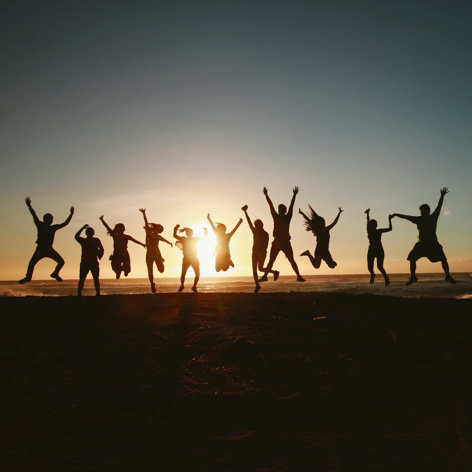 Silhouetten von Menschen, die bei Sonnenaufgang am Strand springen, Gemeinschaft