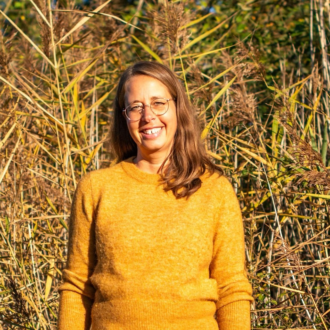 Porträt Nathalie mit Brille, gelbem Pullover vor Naturhintergrund mit trockenen Gräsern