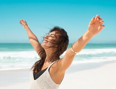 Frau am Strand mit erhobenen Armen, Tinnitus Therapie und Stressabbau