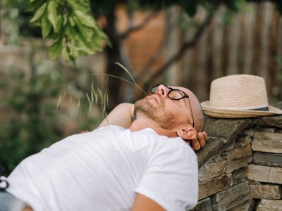 Mann mit Brille und Hut entspannt auf Steinmauer, Achtsamkeitstraining für Tinnitus