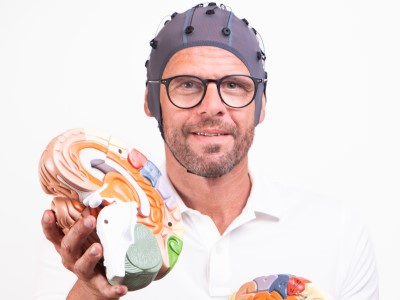 Mann mit EEG-Kappe hält gehirn-förmiges Modell, kognitive Umdeutung Tinnitus-Training