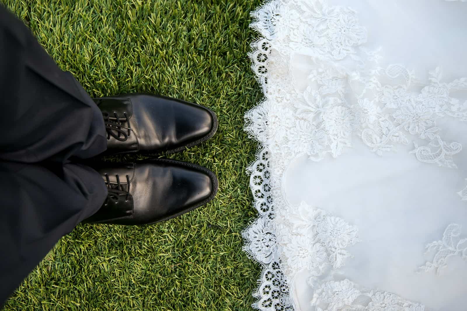 Hochzeitspaar auf grüner Wiese, schwarze Herrenschuhe und weißes Hochzeitskleid, Nahaufnahme von oben