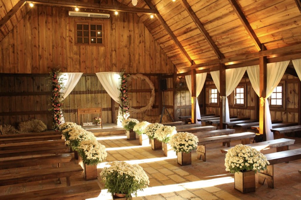 Dekoration einer Scheune zur Freien Trauung mit weißen Stoffen, Blumenarrangements und Holzbalken