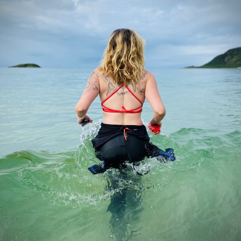 Blonde Frau läuft ins Meer, Blick von hinten, rotes Bikini-Oberteil