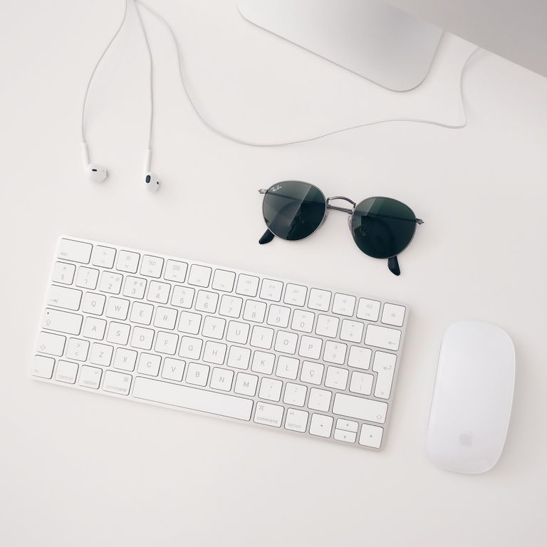 Flatlays Arbeitsplatz mit weißer Tastatur, Maus, Kopfhörern und Sonnenbrille