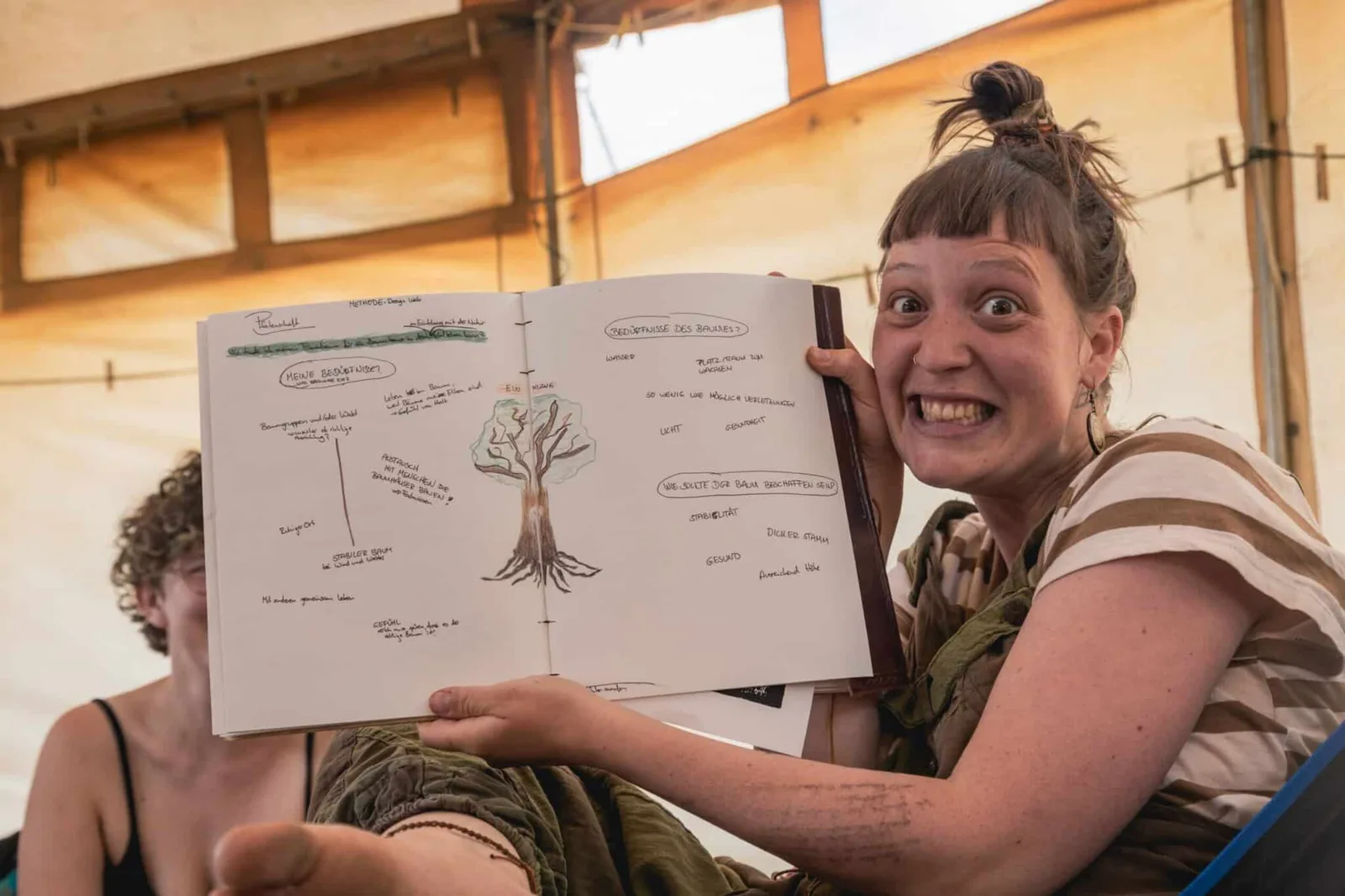 Frau mit Stirnband präsentiert begeistert Skizze mit Baumzeichnung und Notizen zu Wildgestaltung