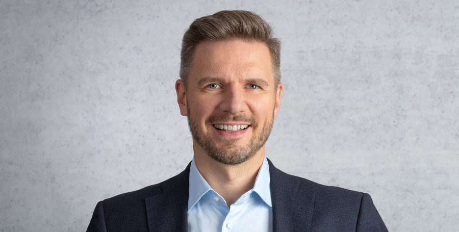 Professionelles Portrait von Ralf Nuppenau in Business-Anzug vor grauem Hintergrund