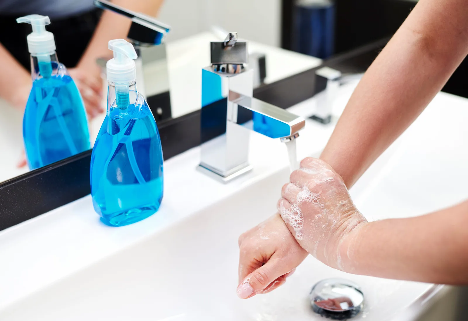 Hände beim Desinfizieren mit blauem Gel an Waschtisch mit Spendern – Hygienemaßnahmen