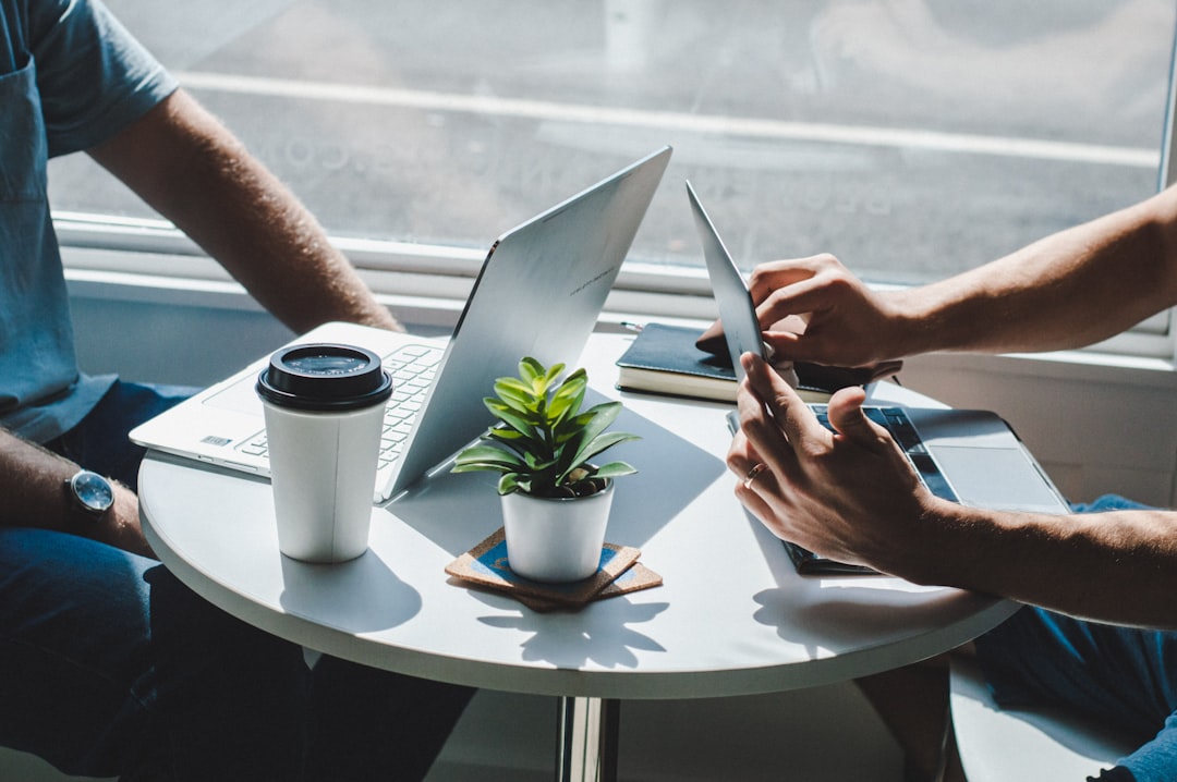 Zwei Personen am Tisch mit Laptop, Kaffee und Pflanze – Zusammenarbeit und Geschäftsbesprechung