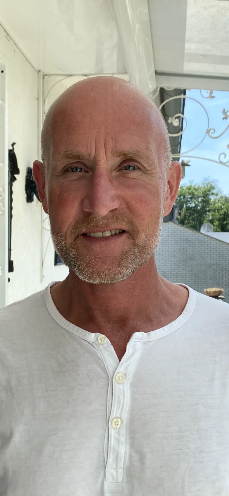 Mann frontal mit Zahnspangen-Lächeln, weiße Henley-Shirt, helles Licht
