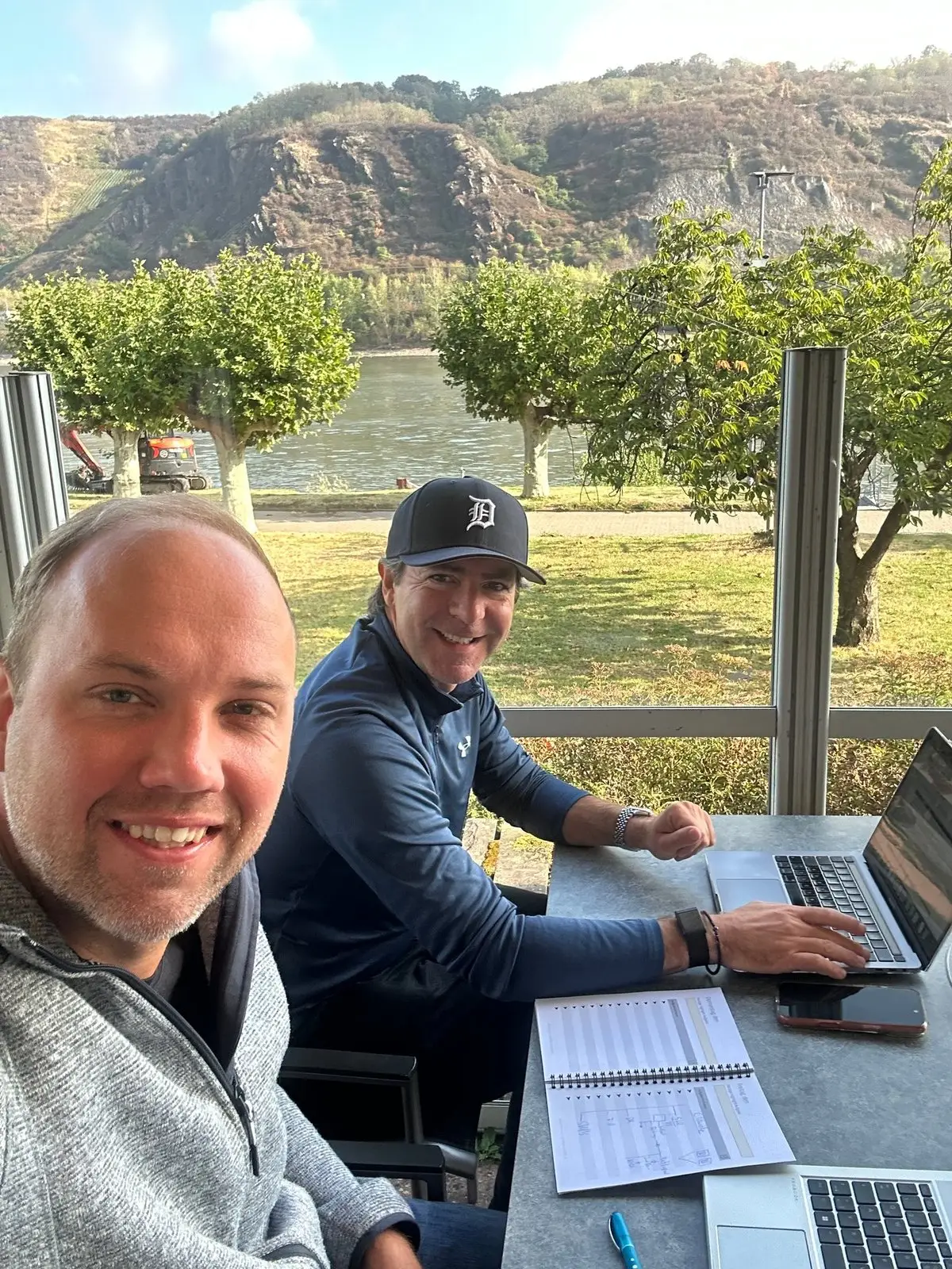 Daniel und Fabian arbeitend am Laptop an Profit Buddies mit Flusslandschaft im Hintergrund