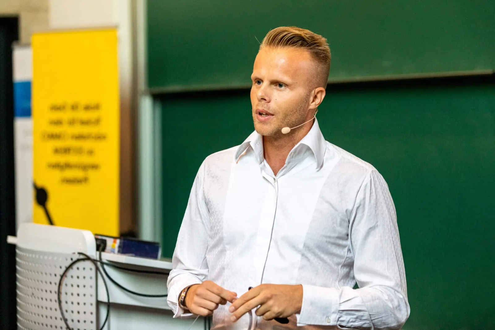 Ronny Barthel spricht vor grüner Tafel mit Headset in weißem Hemd