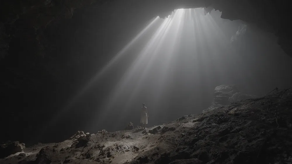 Dunkelgraue Höhlenszene mit dramatischen Lichtstrahlen und silhouettierter Person