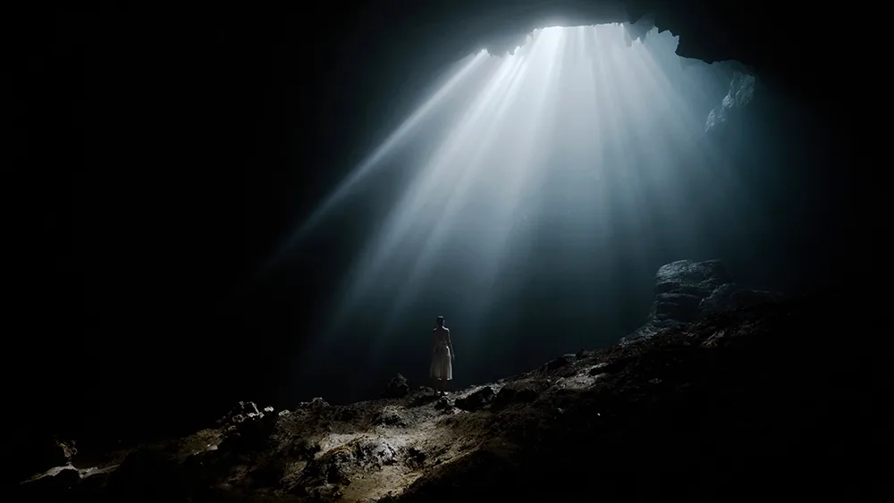 Höhlenszene mit dramatischen blauen und grünen Lichtstrahlen und Person in Silhouette