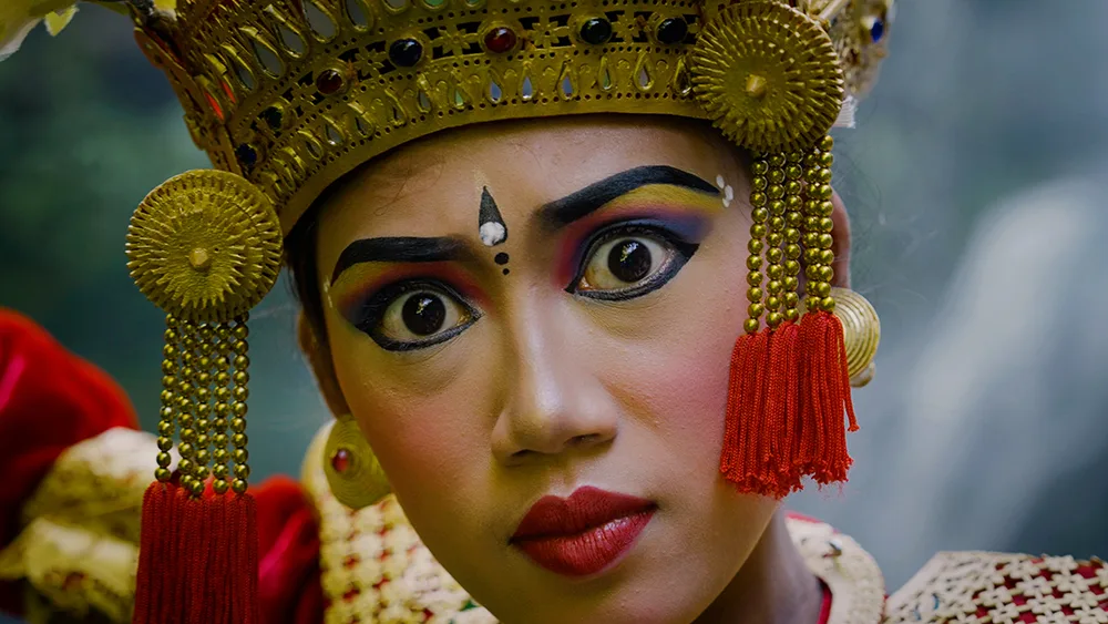 Nahaufnahme weibliches balineses Gesicht mit goldenem traditionellem Kopfschmuck und verschwommenem Hintergrund