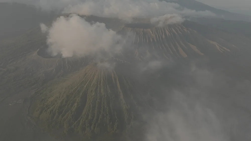 Luftaufnahme von zwei rauchenden Vulkanen mit grünen Hängen in grauer Atmosphäre