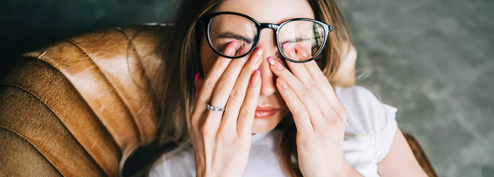 Frau mit Brille hält sich Augen verdeckt, trägt braunes Outfit