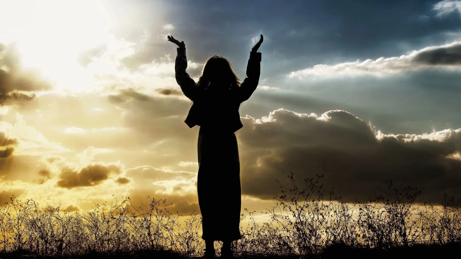 Silhouette einer Frau mit erhobenen Armen vor Himmel und Wolken