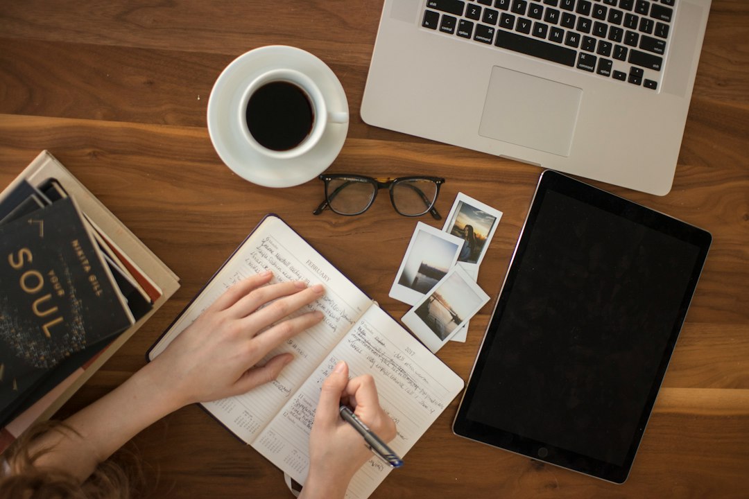 Arbeitsplatz mit Laptop, Kaffee, Notizbuch und Brille auf Holztisch