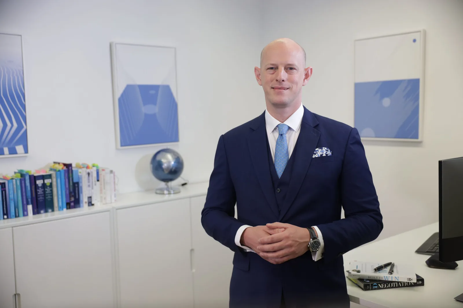 Dr. Alexander Hoeppel im Büro neben Schreibtisch mit Bücherregal und Globus