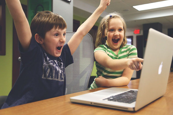 Zwei Kinder jubeln begeistert vor Laptop am Tisch