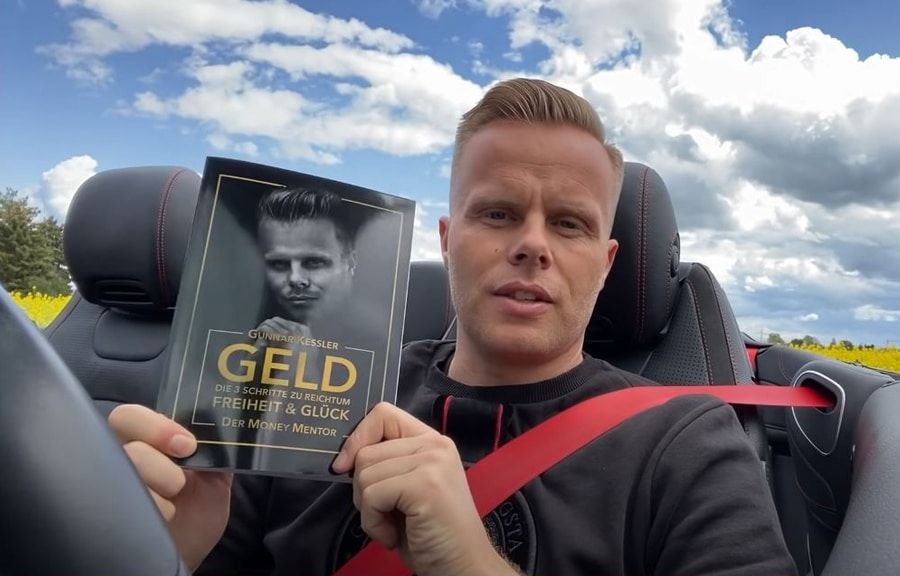 Gunnar Kessler hält sein Geld-Buch im Cabrio in die Kamera