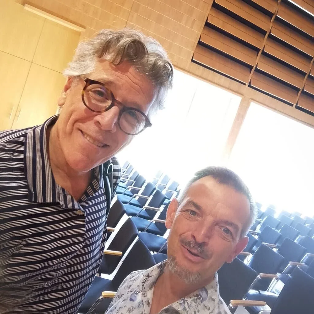 Zwei Männer lächelnd im Konzertsaal, einer mit Brille im gestreiften Hemd, Thomas Hampson und Robert Sawilla