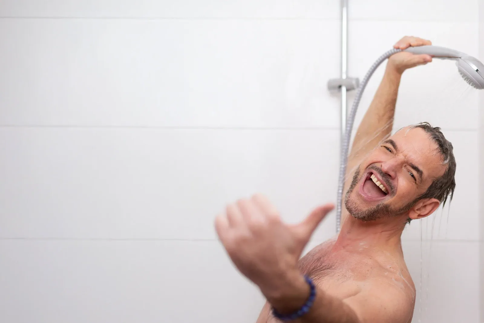 Mann unter der Dusche mit erfreuter Mimik, Wasser läuft über Gesicht und Körper