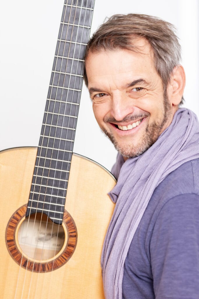 Robert Sawilla, Vocal-Coach und Stimmtherapeut, mit Akustikgitarre in lila Hemd