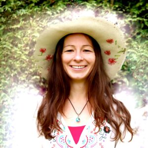 Lächelnde Frau mit braunen Haaren, Cowboy-Hut und pinkem Triangel-Muster auf weißem Oberteil
