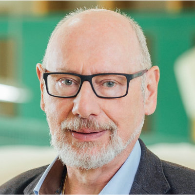 Porträt Günther Amann-Jennson, älterer Mann mit Brille vor grünem Hintergrund