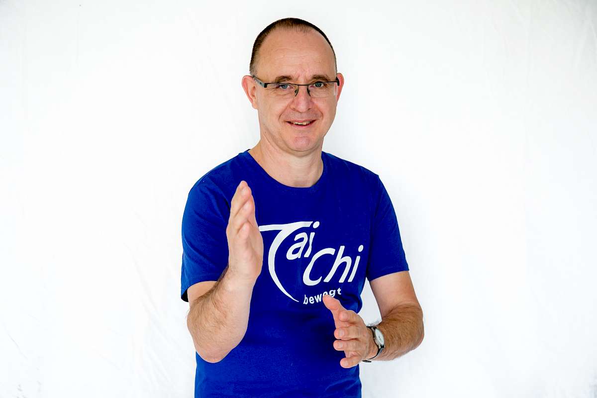 Dirk Ortlinghaus in blauem Tai Chi bewegt Shirt zeigt Qigong-Bewegung, Portraitfoto