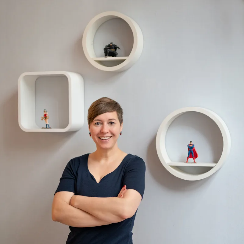 Susanne Lorenz lächelnd vor weißer Wand mit weißen Regalnischen, die Arme verschränkt