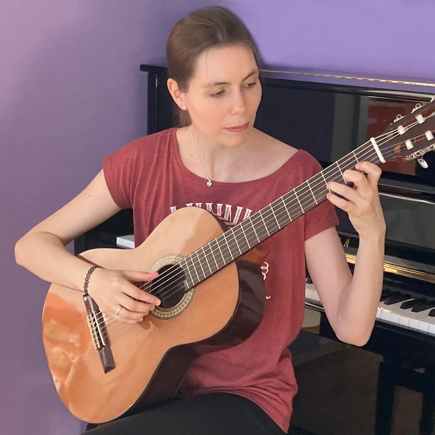 Frau in Bordeaux-Shirt spielt Akustikgitarre vor violettem Hintergrund
