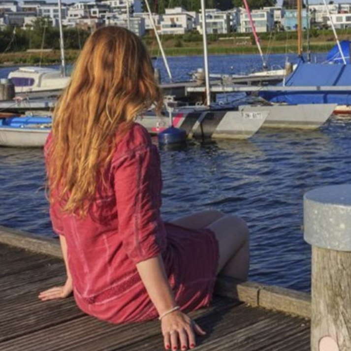 Frau mit langen rötlichen Haaren am Bootssteg mit Segelbooten
