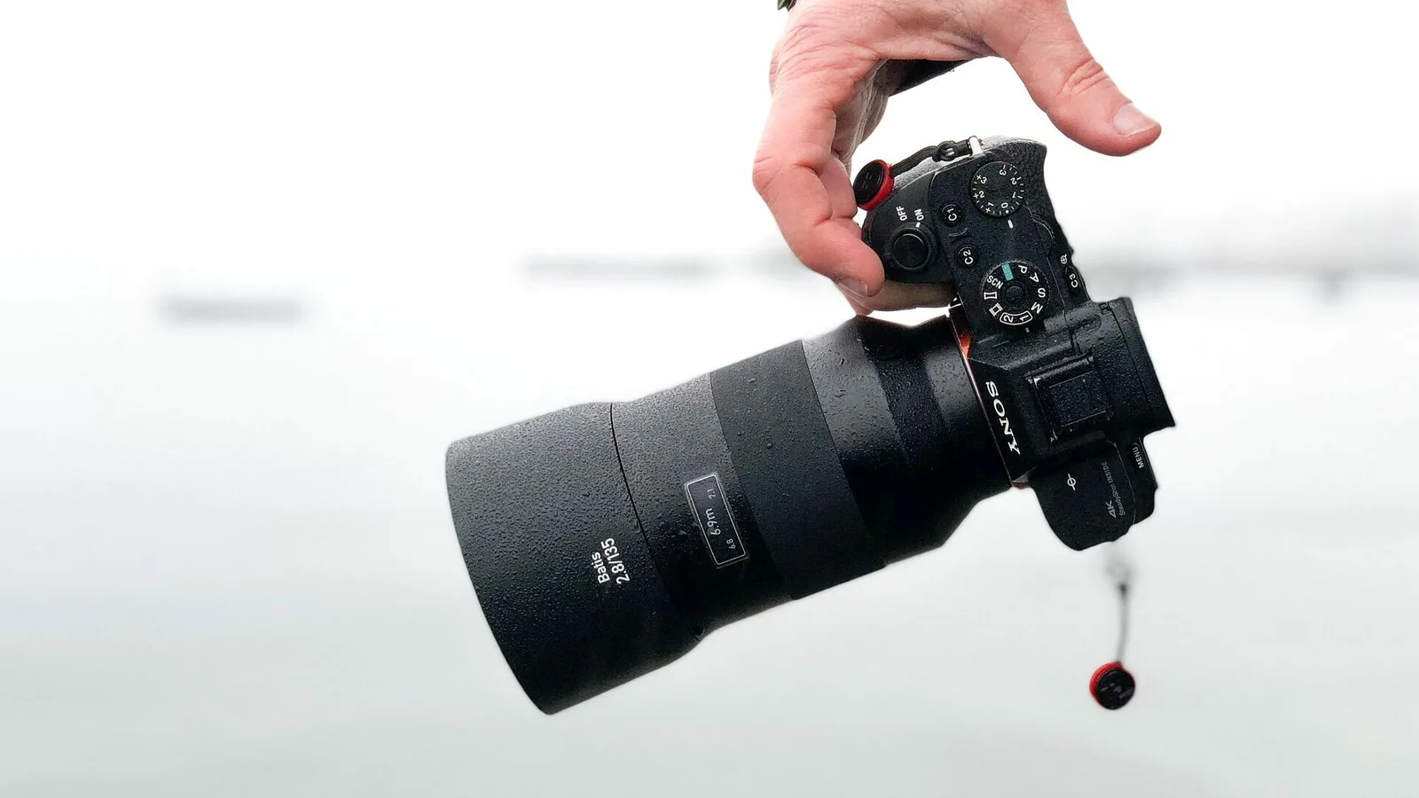 Professionelle Videokamera mit Zoomobjektiv in Handposition auf weißem Hintergrund