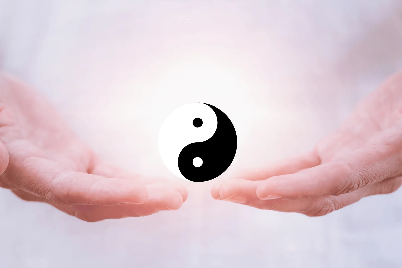 Yin-Yang-Symbol in Schwarz-Weiß, umrahmt von zwei Händen auf hellem, verschwommenem Hintergrund