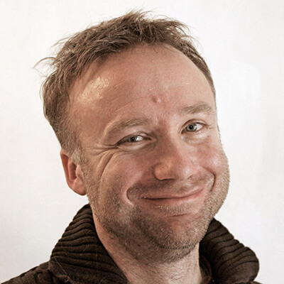Porträtfoto von Dr. Weidinger, Mann mit braunen Haaren und braunem Hemd vor hellem Hintergrund