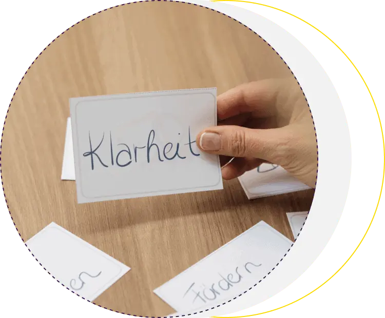 Goldrichtig – Videokurs zu wertebasierter Führung 7 Hand hält Karteikarte mit Wort 'Klarheit' auf Holztisch, goldener Kreis-Rahmen