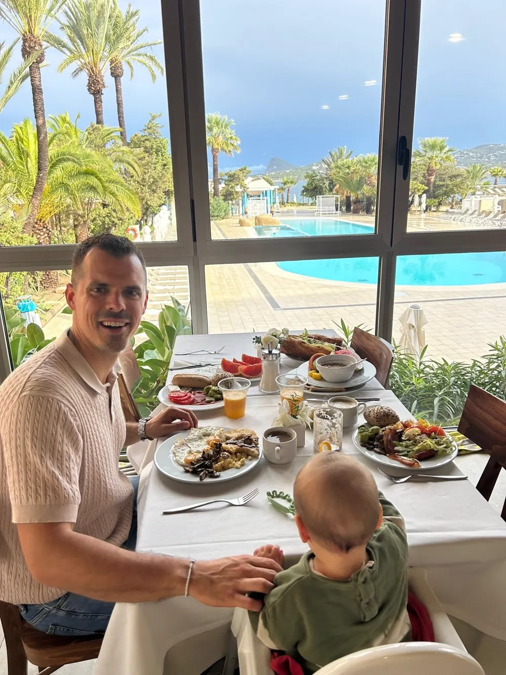 Vater und Kind frühstücken am Pool mit Palmenbäumen und Meerblick im Hintergrund