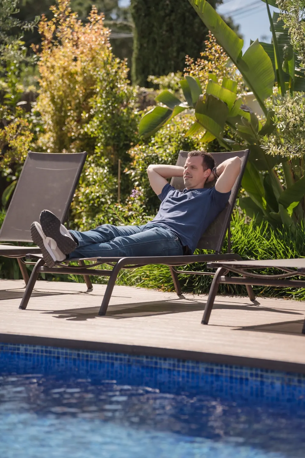 Mann entspannt auf Sonnenliege am Pool mit Blick auf Garten und Wasser