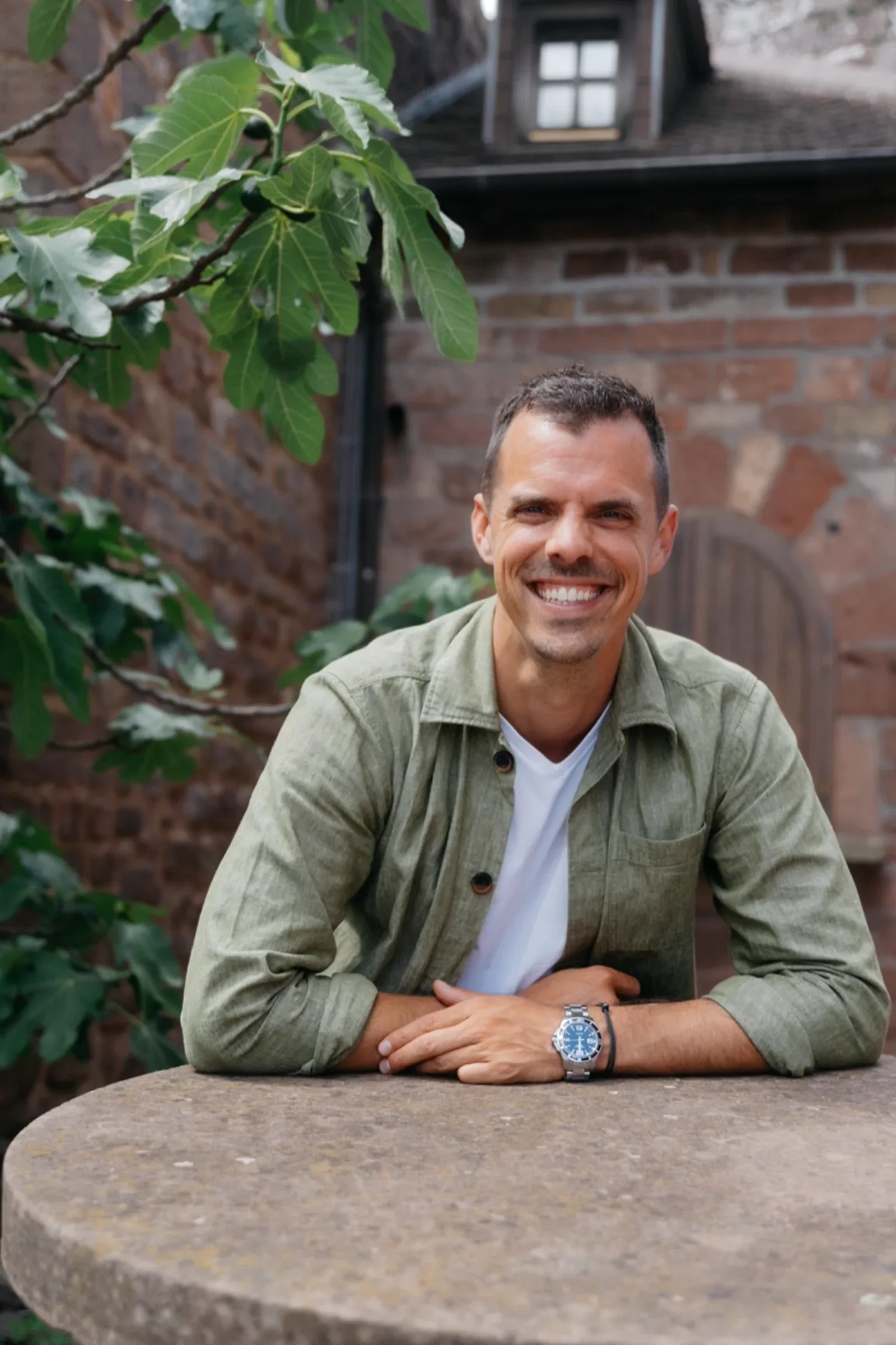 Jens Neubeck, Mitgründer der Sales Angels, lächelnd am Tisch vor Backsteinwand