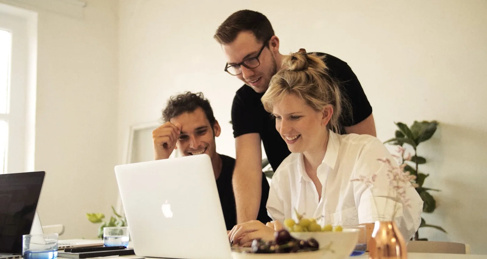Team von drei Personen arbeitet gemeinsam an Laptop in modernem Büro mit Pflanzen